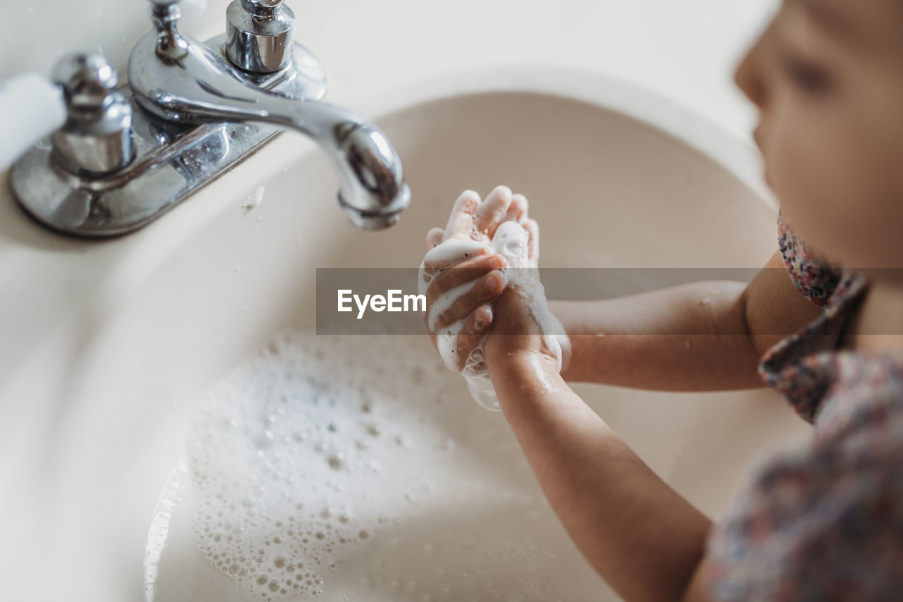 High angle view of young girl washing hands in sink with soap