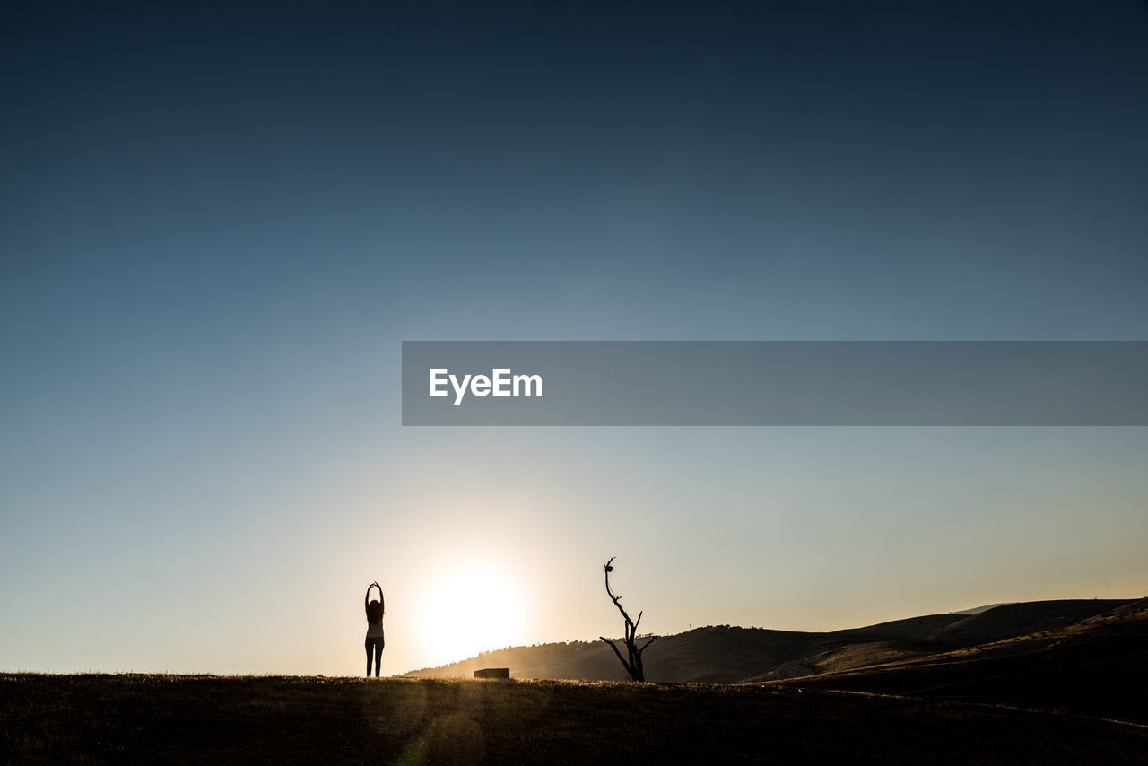 Silhouette woman standing on landscape against sky during sunset