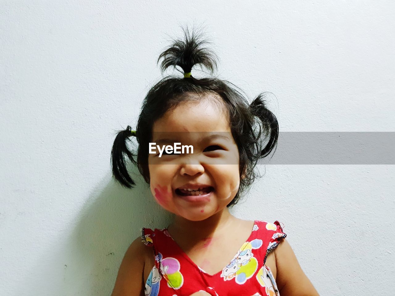 Portrait of cute smiling baby girl with pigtails against wall