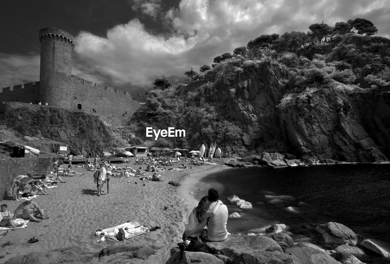 Rear view of man and woman sitting on rock at shore