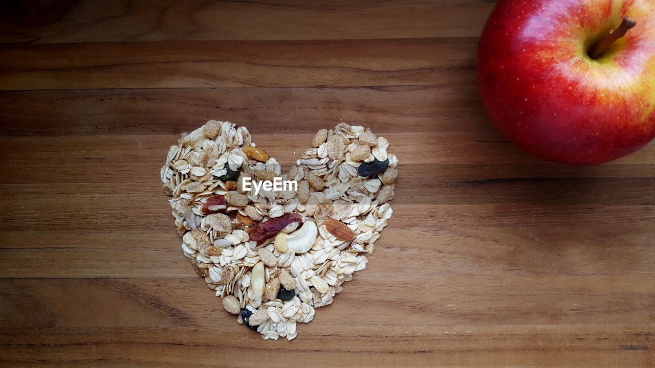 High angle view of heart shape made from breakfast cereals by apple on wooden table