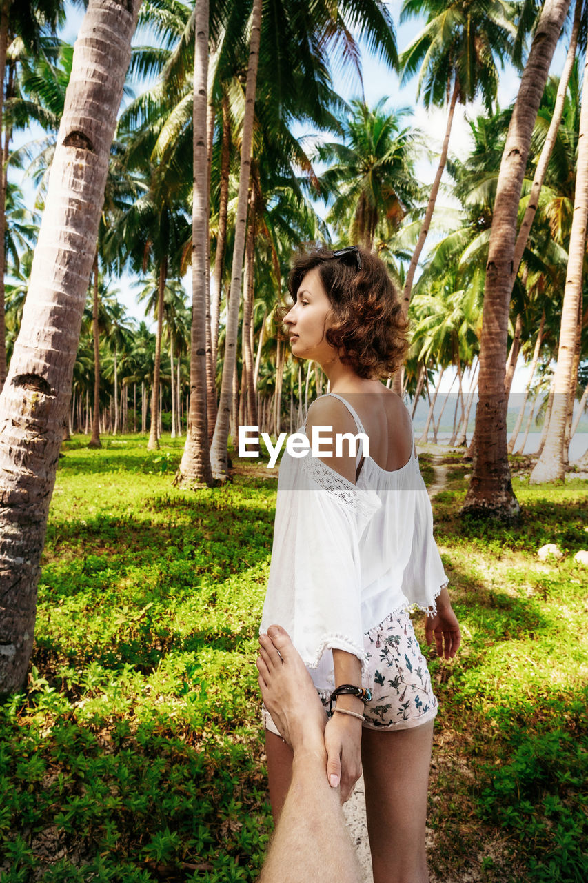 FULL LENGTH OF YOUNG WOMAN STANDING BY TREE