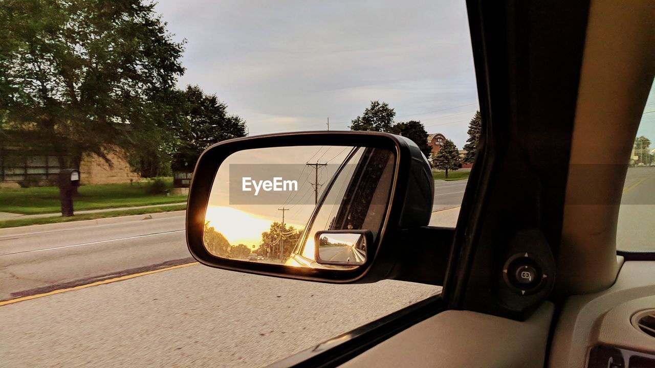 Reflection of car on side-view mirror against sky