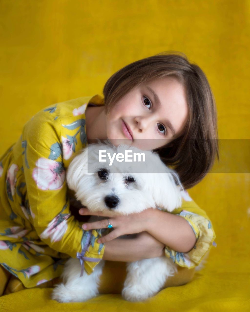 Portrait of cute girl embracing white puppy against yellow background