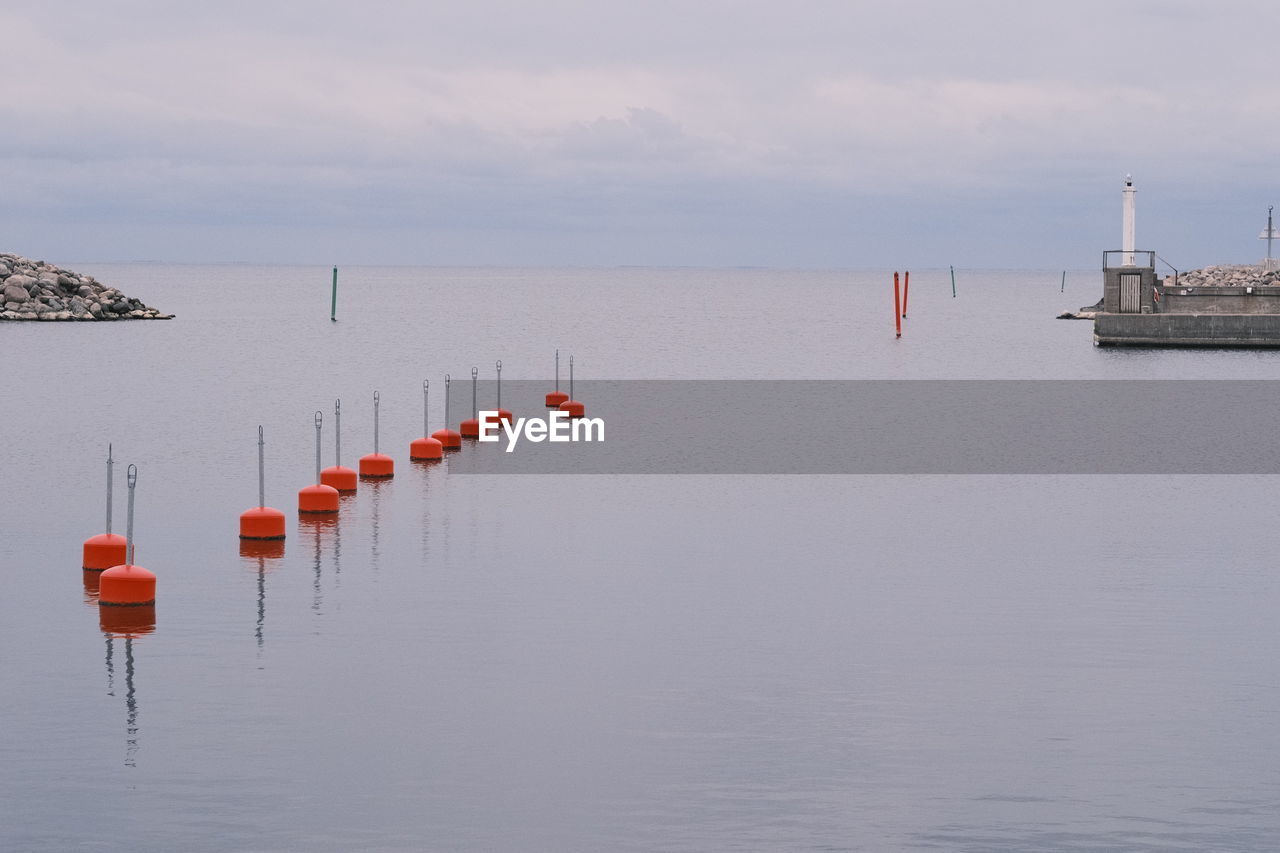 water, sea, sky, vehicle, nature, nautical vessel, transportation, tranquility, beauty in nature, scenics - nature, tranquil scene, no people, buoy, cloud, shore, pier, day, reflection, architecture, ocean, horizon over water, outdoors, mode of transportation, boat, travel, post, wooden post, bay, in a row, environment, waterfront, built structure, horizon, non-urban scene, beach, ship, coast, idyllic, travel destinations, channel, landscape, seascape