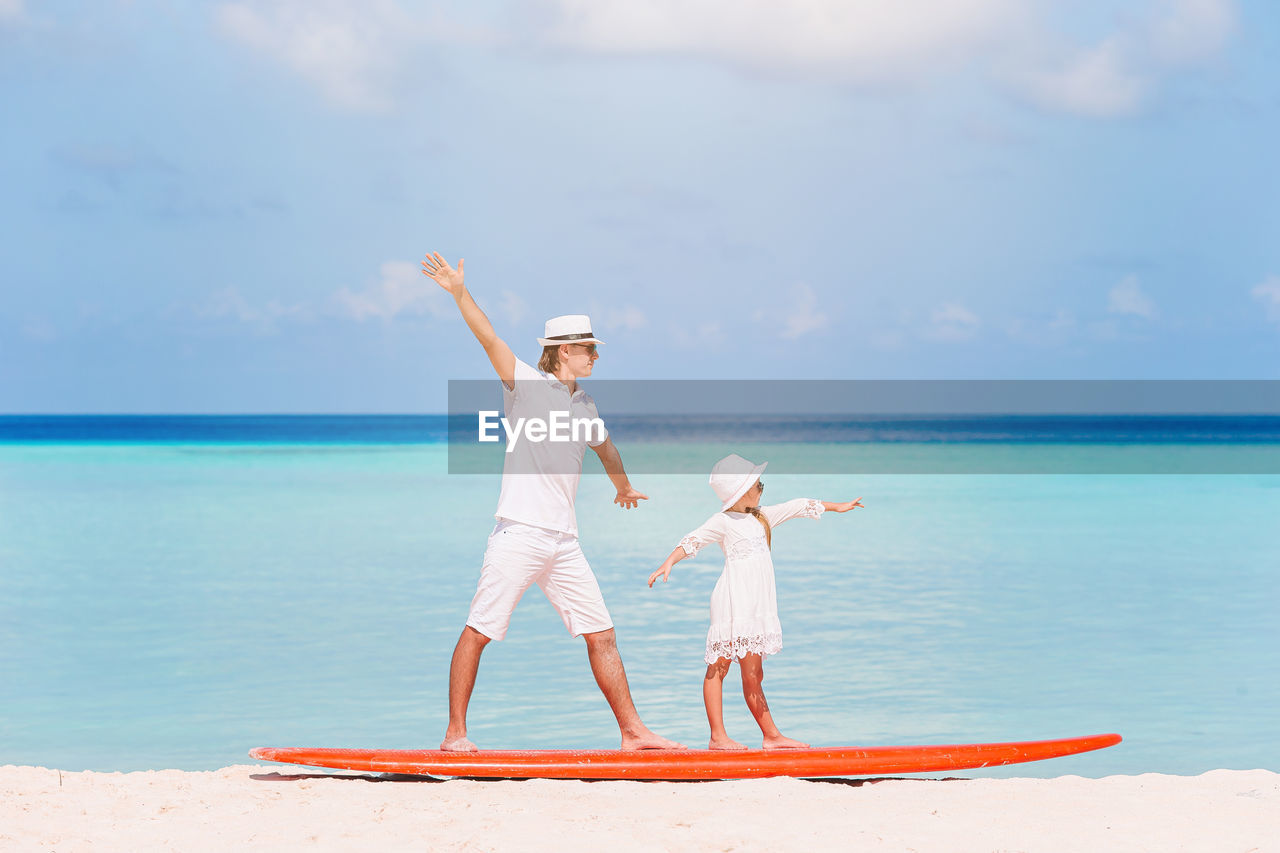 Full length of father and daughter standing on paddleboard