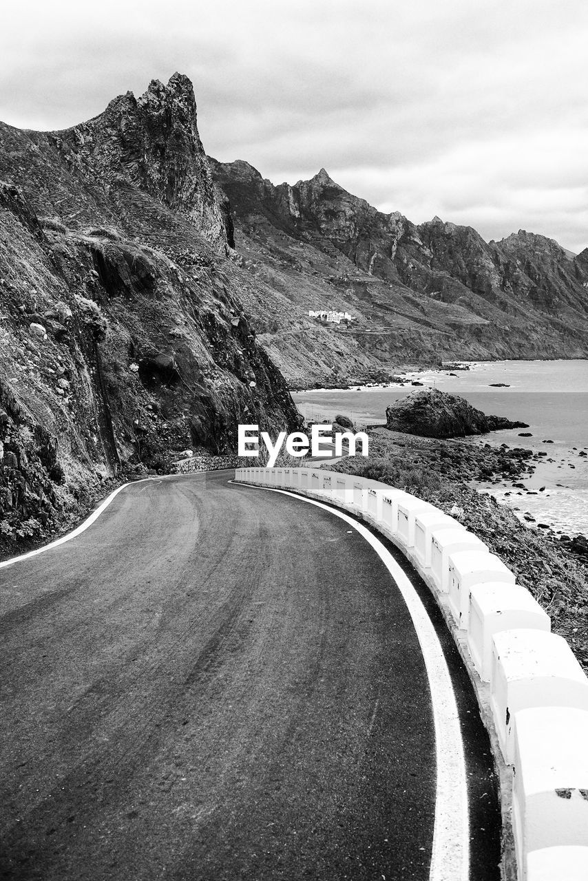 Empty road by mountain against cloudy sky