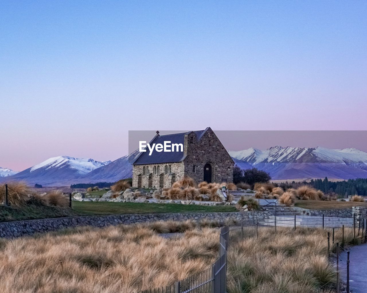 Houses on field by snowcapped mountains against clear blue sky