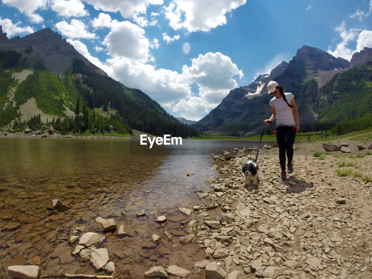 Young woman walking with dog at lakeshore against mountains