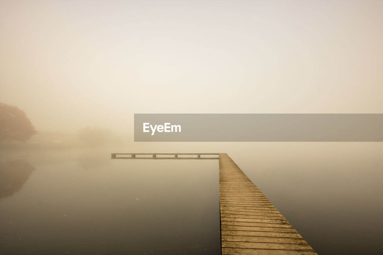 Pier over lake against sky during foggy weather