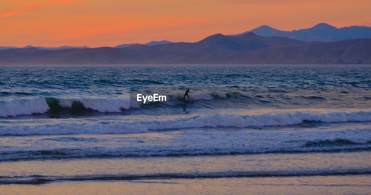 SCENIC VIEW OF SEA BY MOUNTAINS AGAINST SKY DURING SUNSET