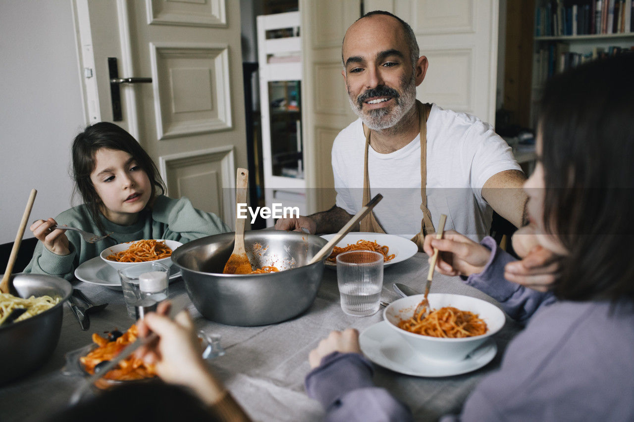 Happy father eating spaghetti with children at dining table