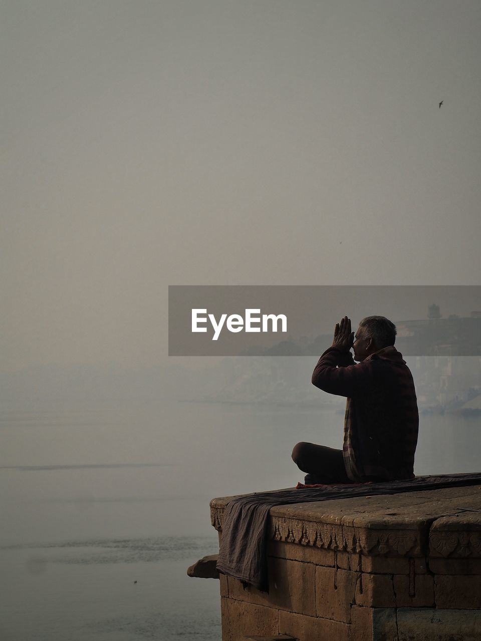 Man praying while sitting by sea against sky