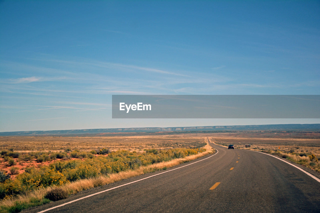 Road passing through landscape against clear blue sky