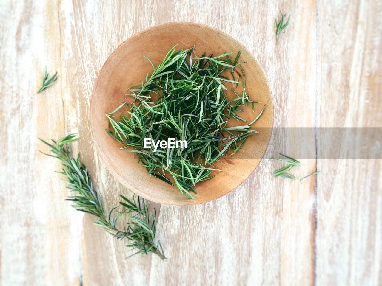 Top view of fresh rosemary in bowl on wooden table