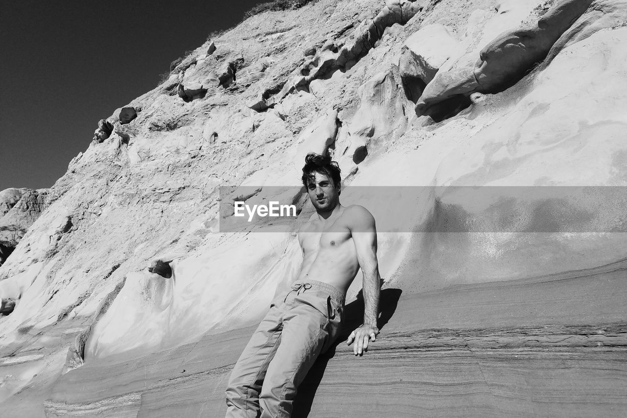 Low angle view of shirtless man standing by rock formation