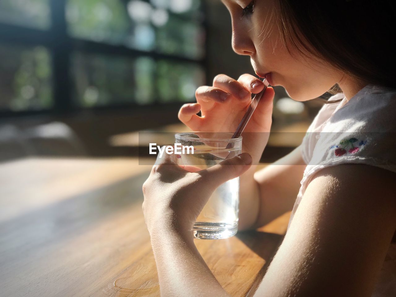 Profile view of girl drinking water while sitting at table