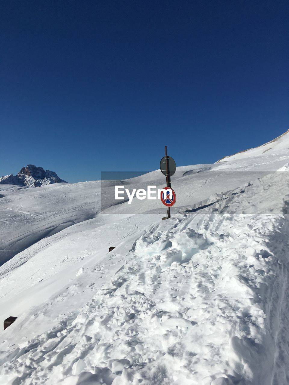 Road mark on snowcapped mountain against clear blue sky