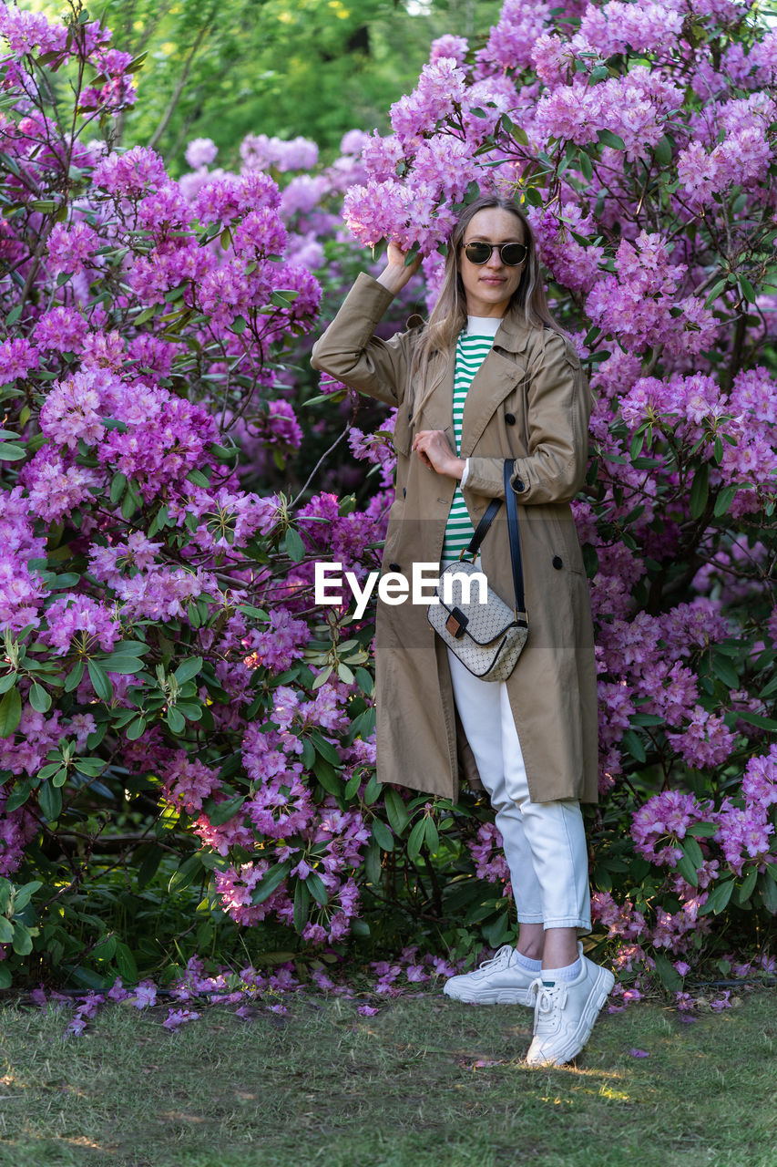 Long-haired woman in sunglasses vohle of a lushly blooming rhododendron bush