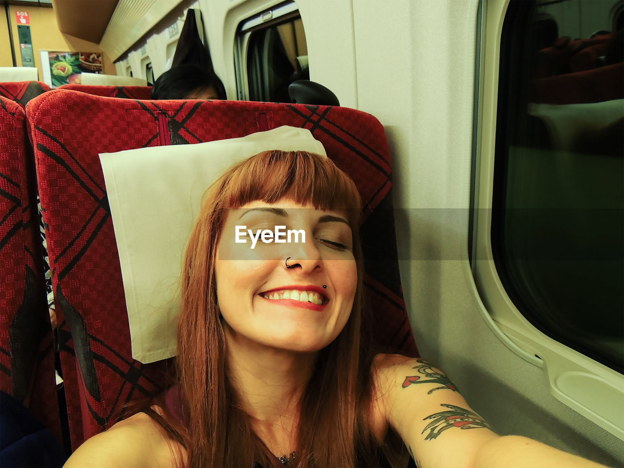 Self-portrait of a young traveler with red straight hair smiling with eyes closed inside of a train