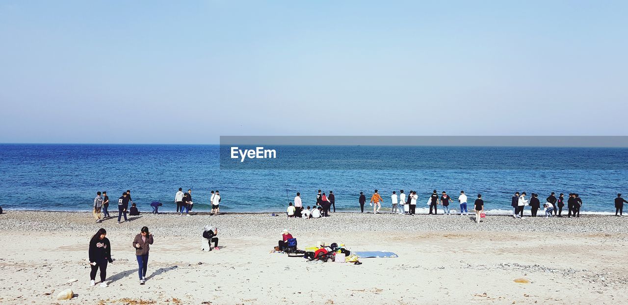 Group of people at beach against clear sky