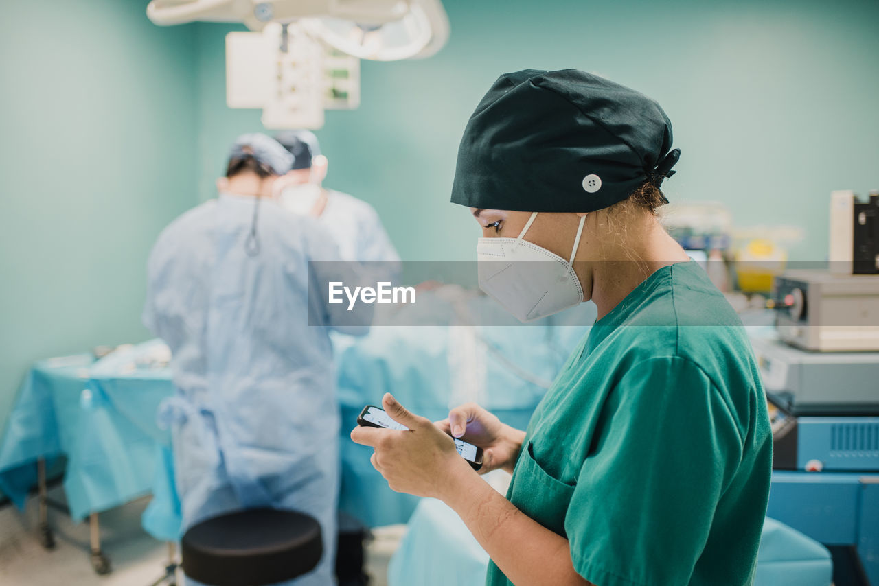 Female nurse using mobile phone inside operation room at modern hospital - focus on woman face