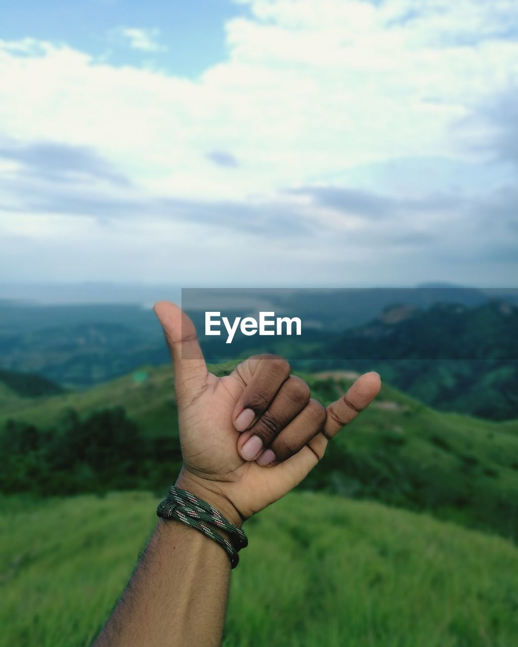 Cropped hand gesturing shaka sign against landscape