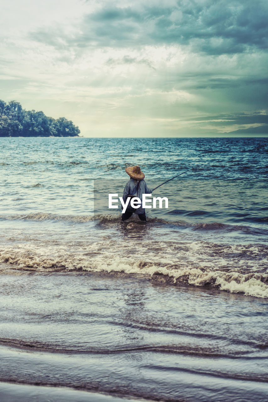 Fisherman standing in sea against sky