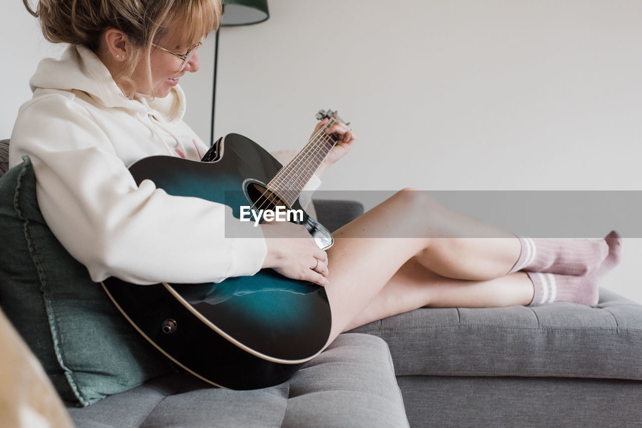 Woman sat on the couch playing guitar smiling