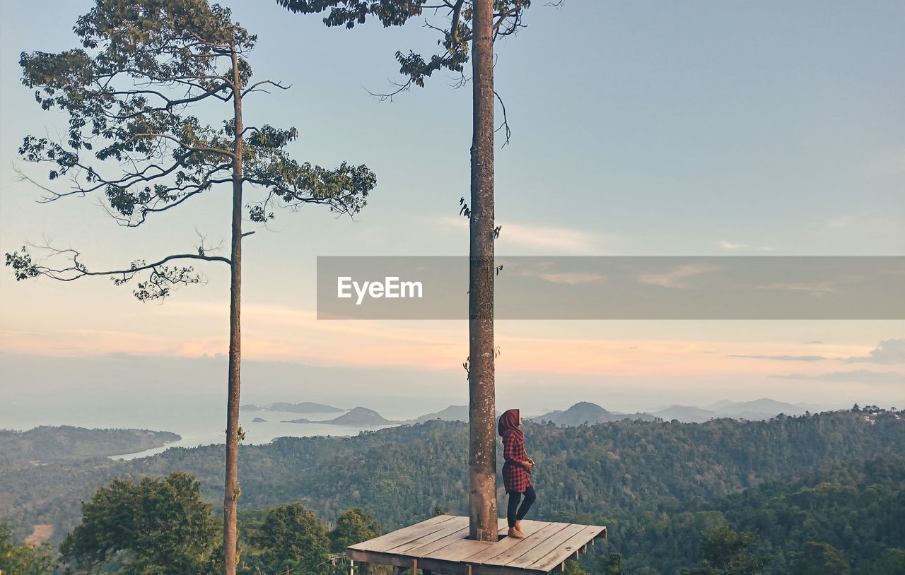 Women standing by tree against sky during sunset