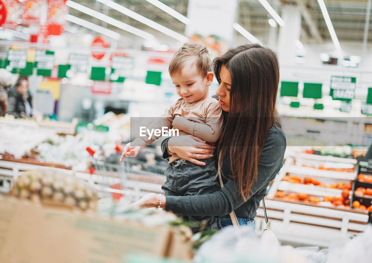 Young woman with baby boy standing in supermarket