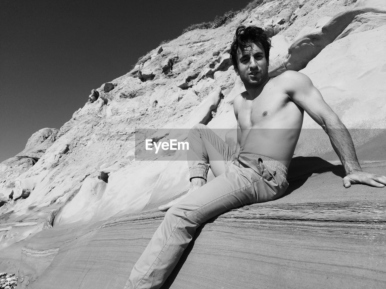 Portrait of shirtless young man sitting on rock formation