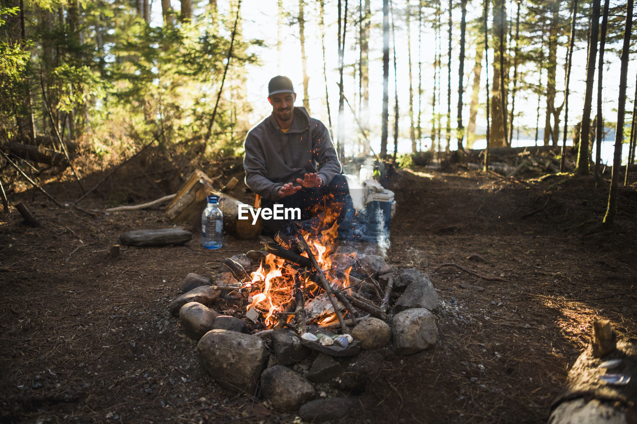 Man warming by the fire at sunset while car camping in coastal maine