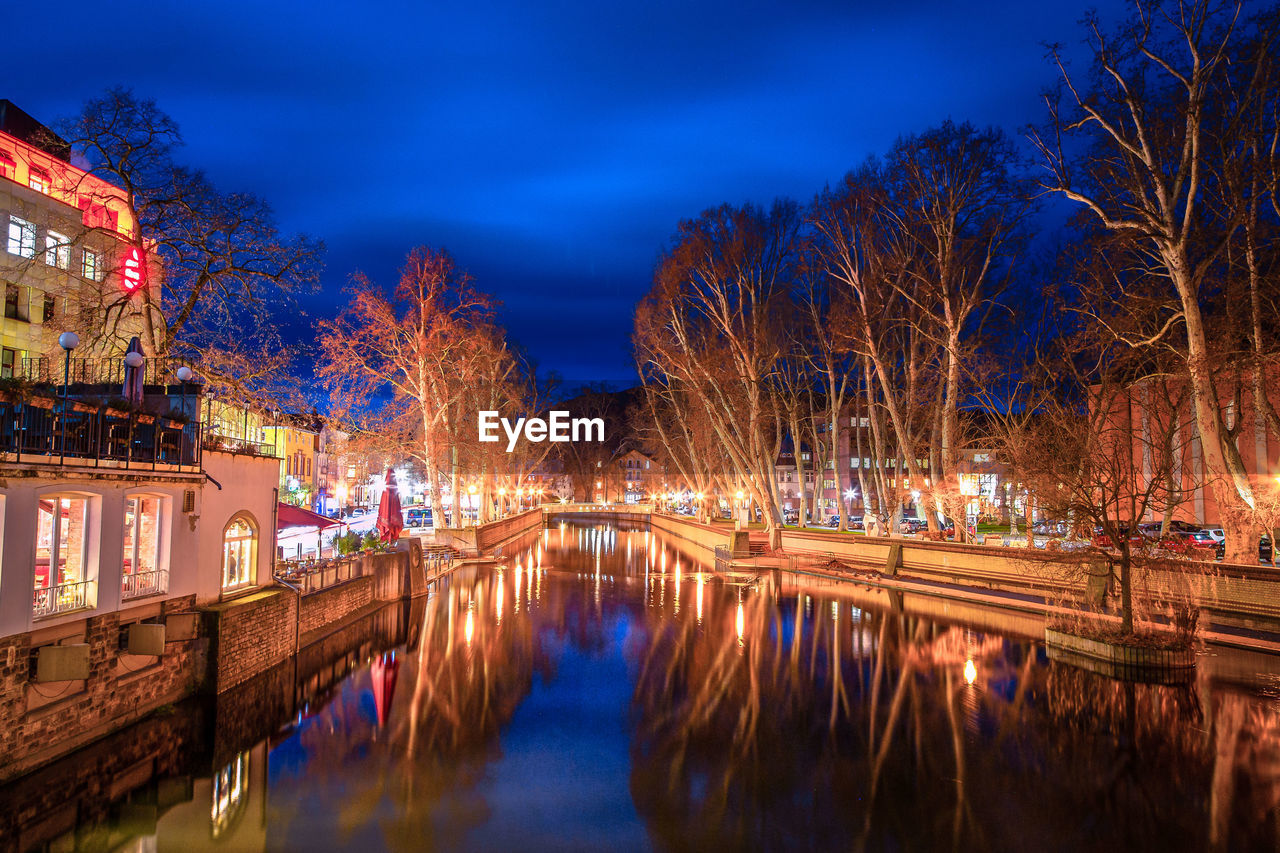 Illuminated buildings by river against sky at night