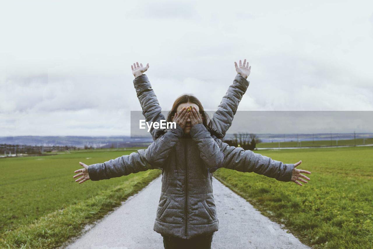 Children standing with arms outstretched on field against sky