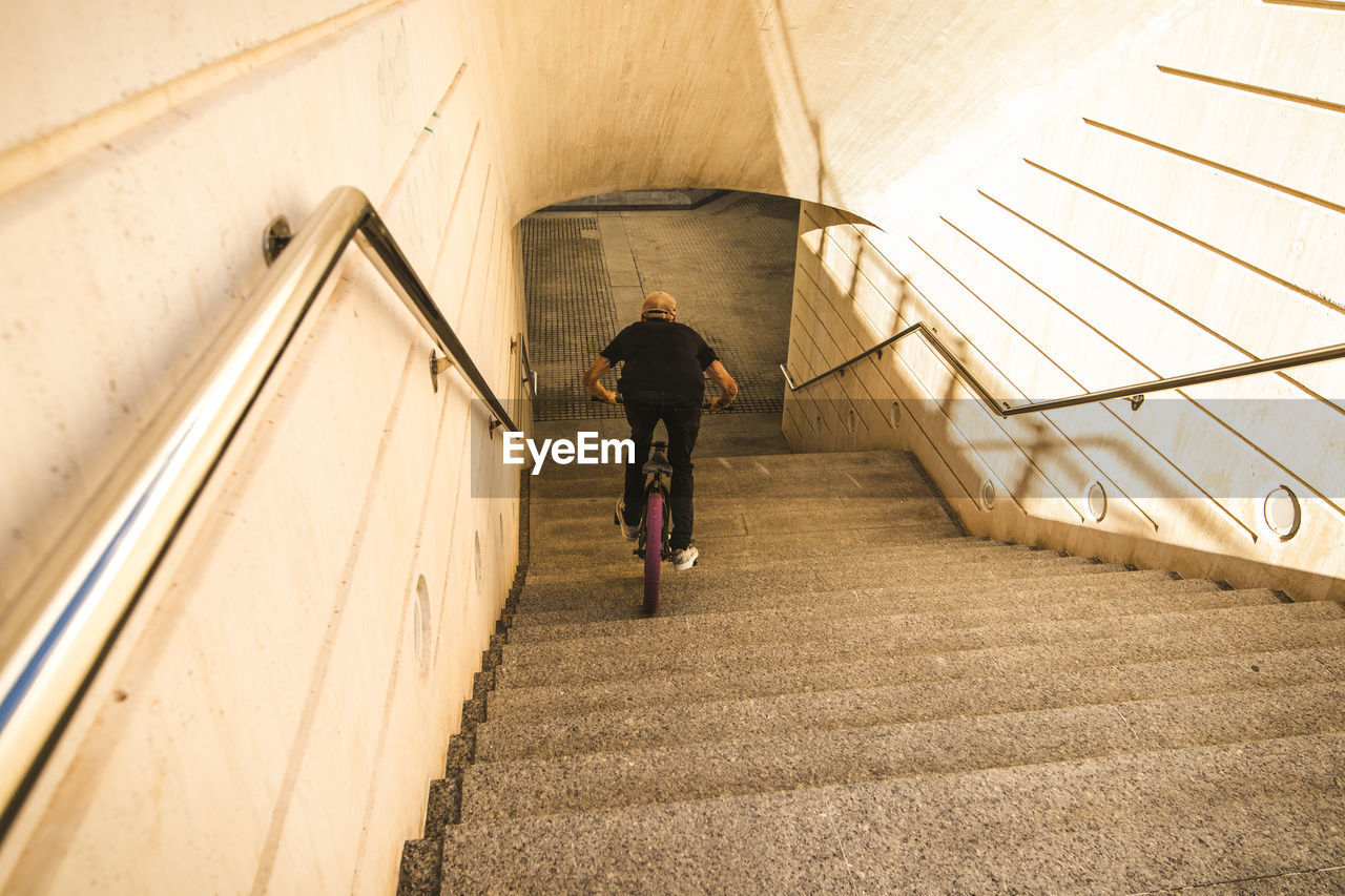 Rear view of young man riding bicycle on steps