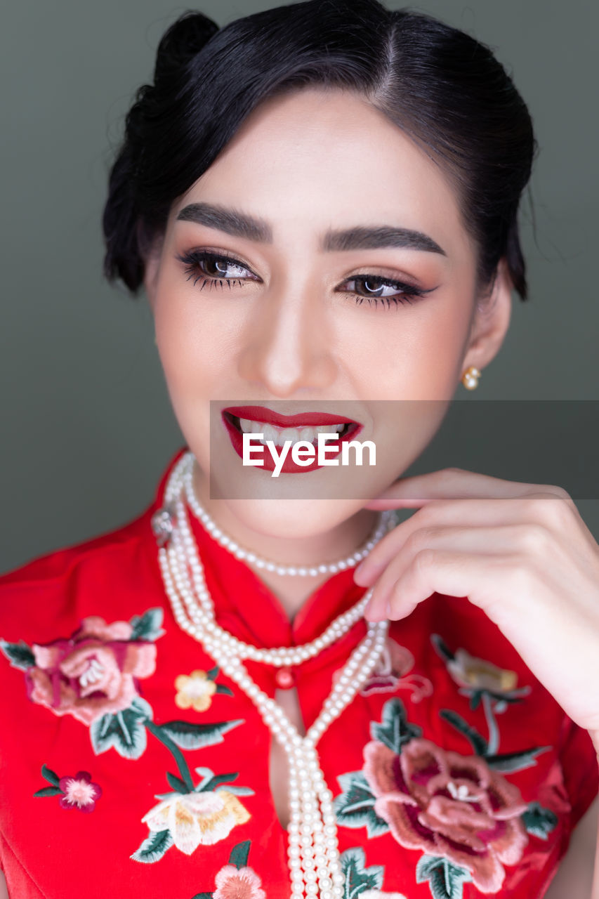 Smiling woman wearing make-up and traditional clothing against gray background