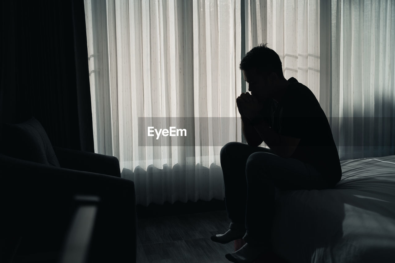 Silhouette man sitting against window at home