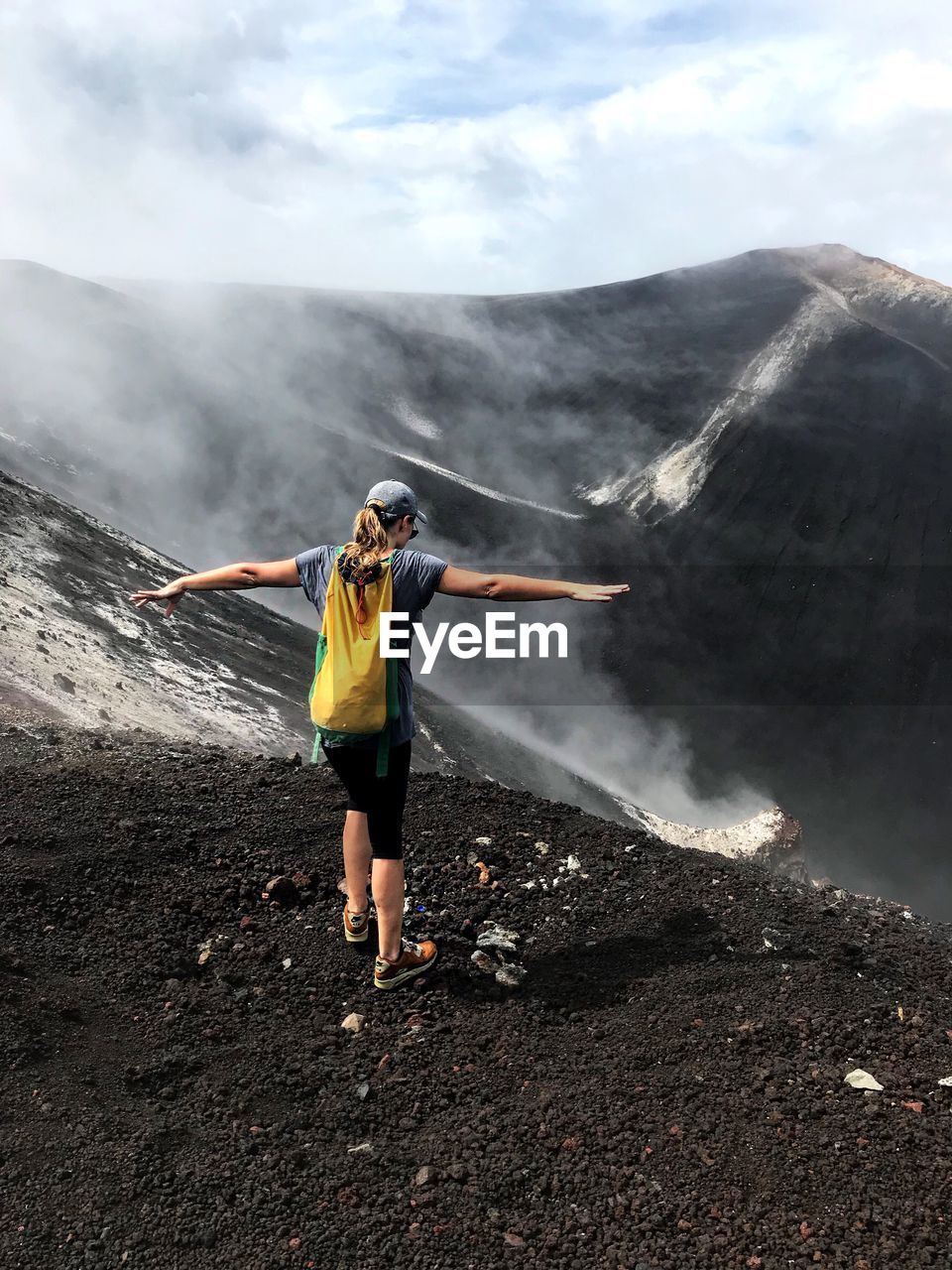 Rear view of woman standing with arms outstretched at volcanic crater
