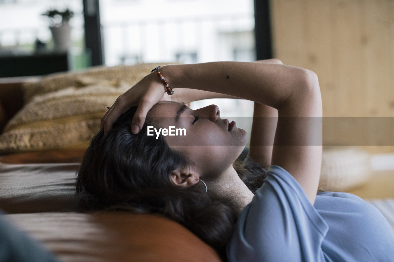 Side view of depressed woman with hand in hair reclining on sofa at home