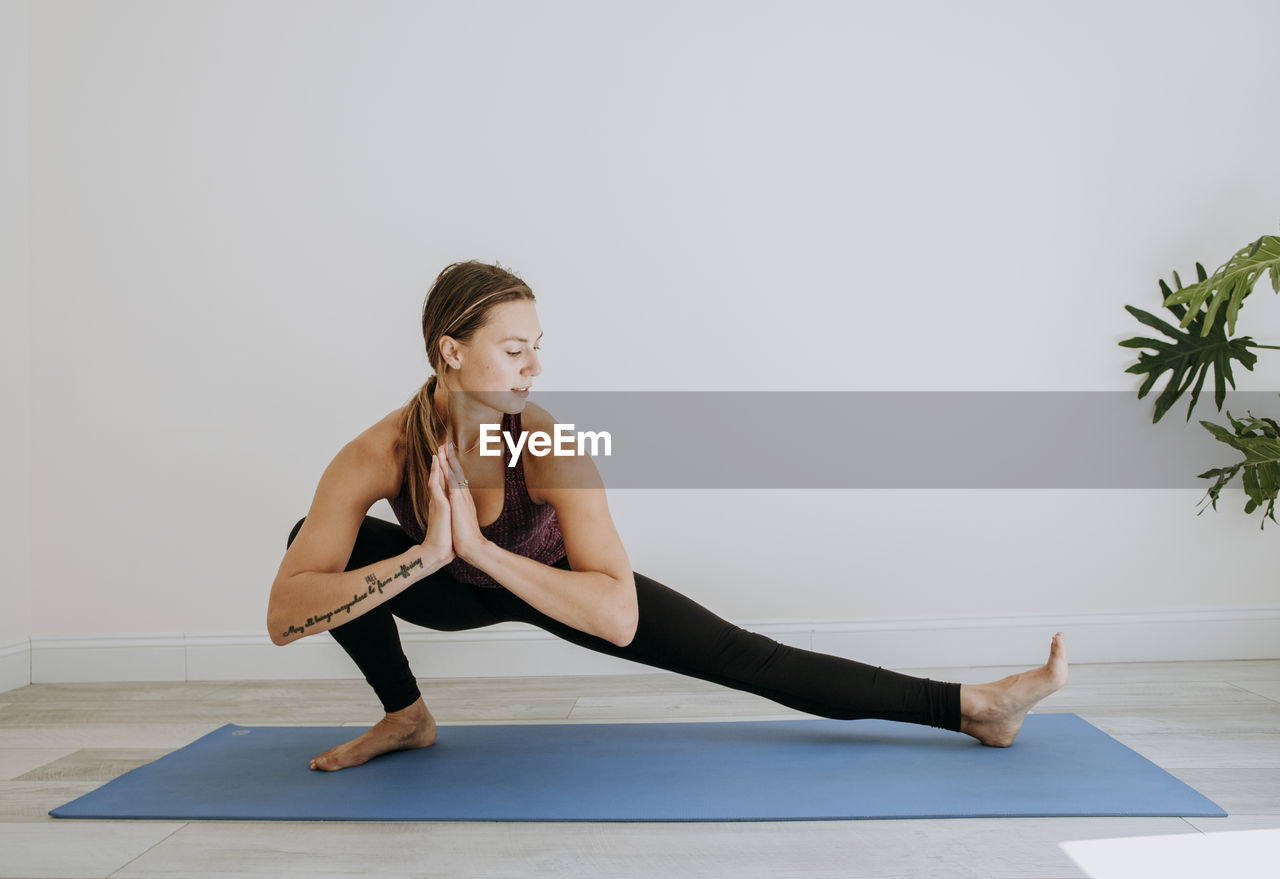 Woman with hands together practices yoga in white simple room