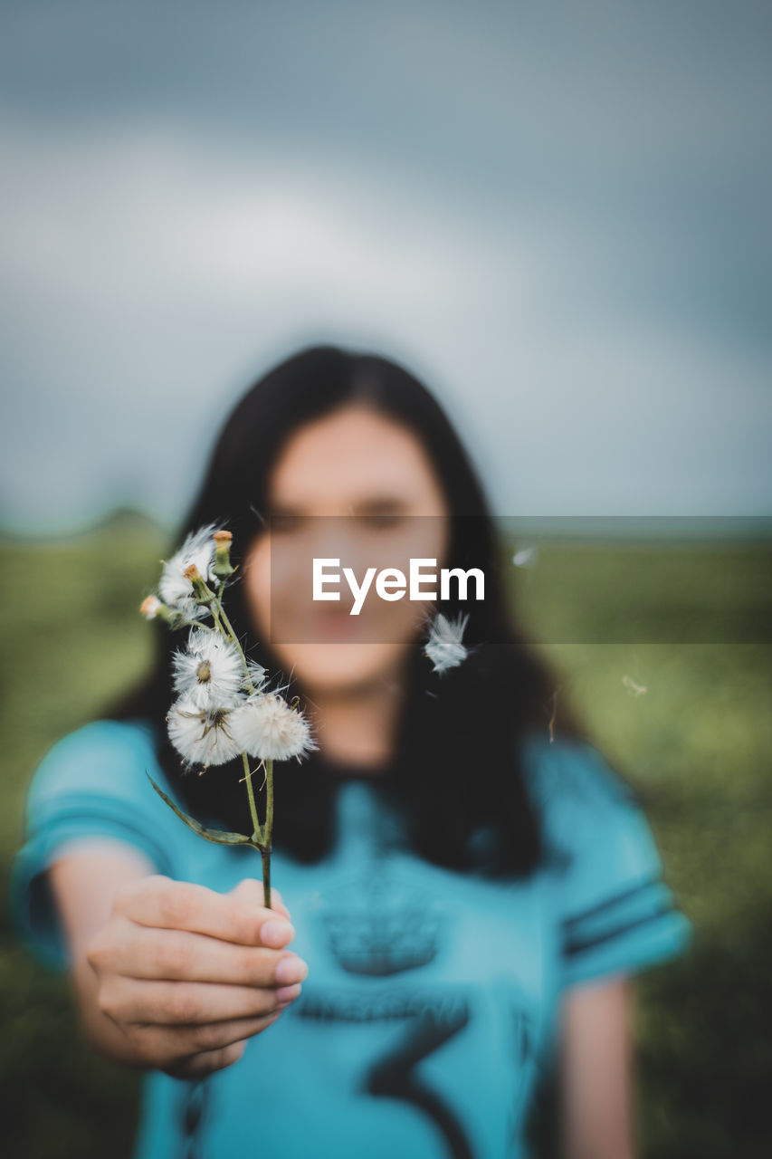 Woman holding dandelion flower against sky