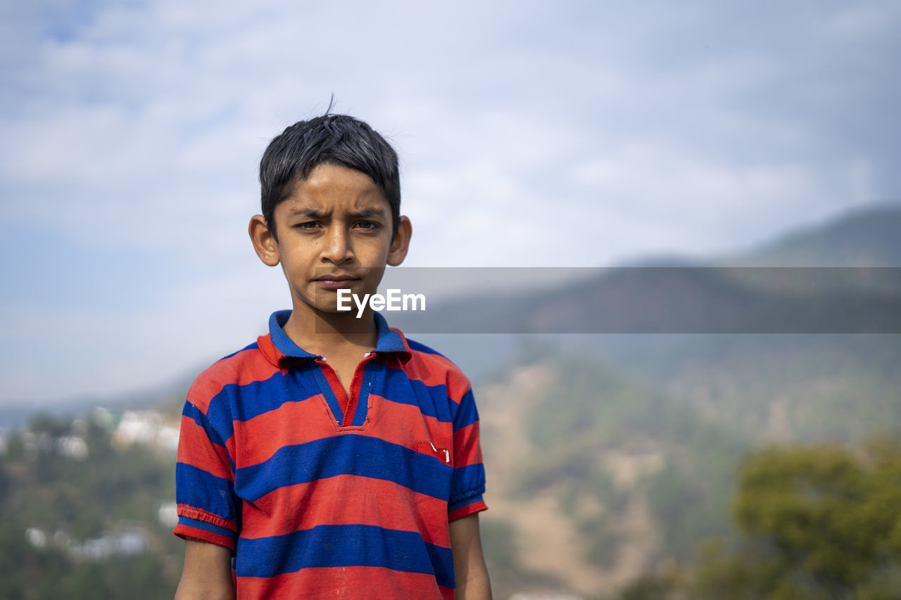 Portrait of a young kid looking into the camera, with blurred mountains in the background.