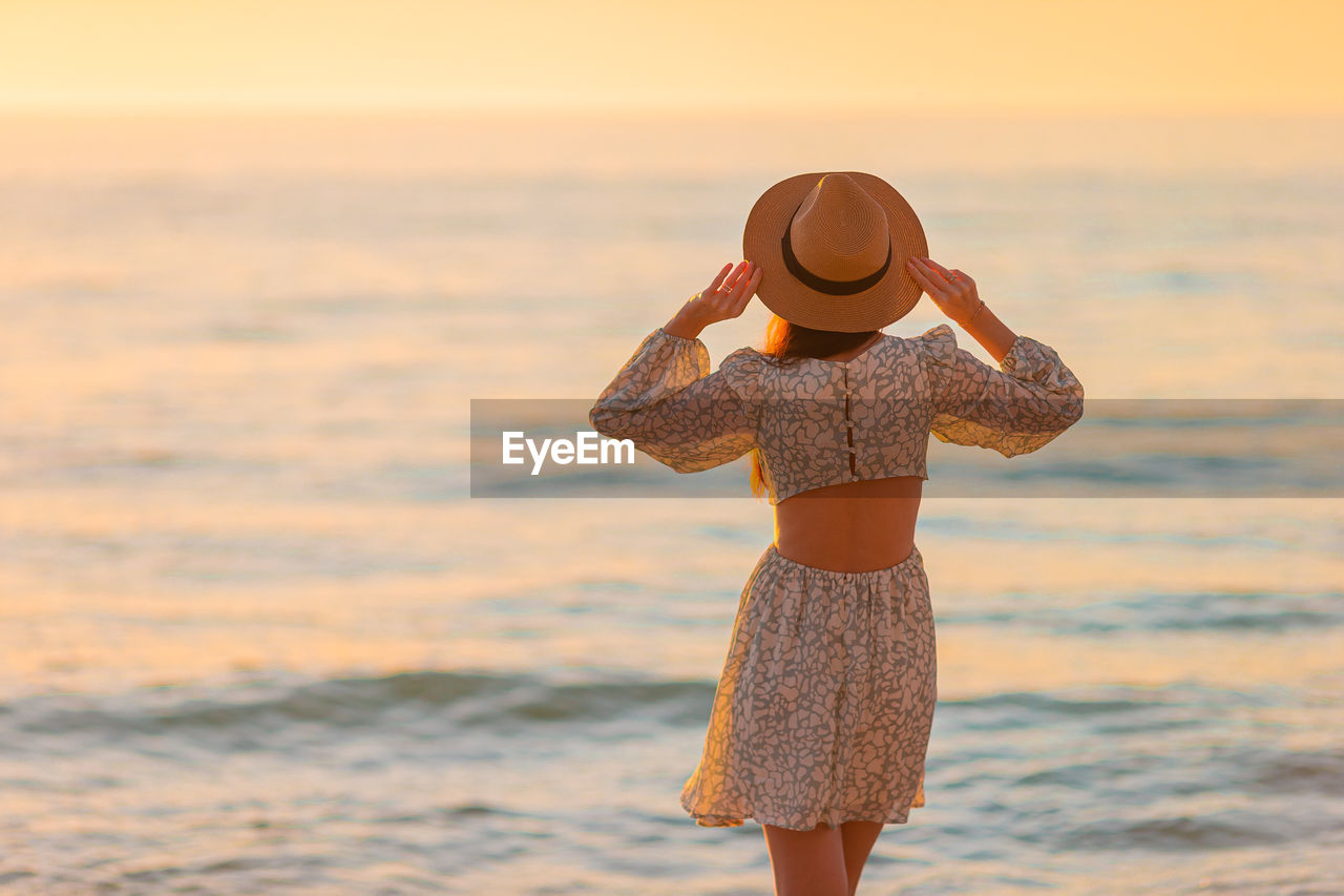 rear view of woman wearing hat while standing at beach