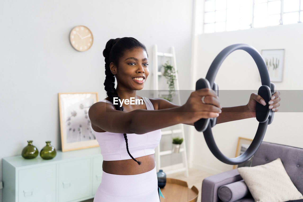 Smiling woman exercising with pilates ring at home
