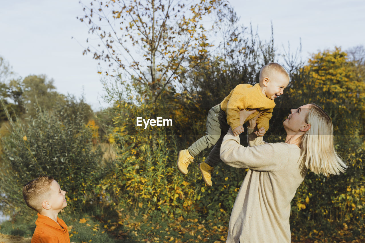 Happy boy looking at mother carrying son in autumn