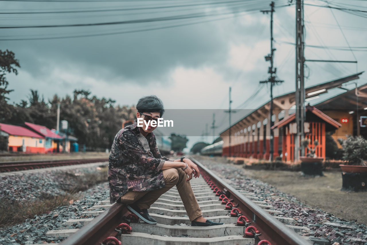 Side view of man sitting on railroad track against sky