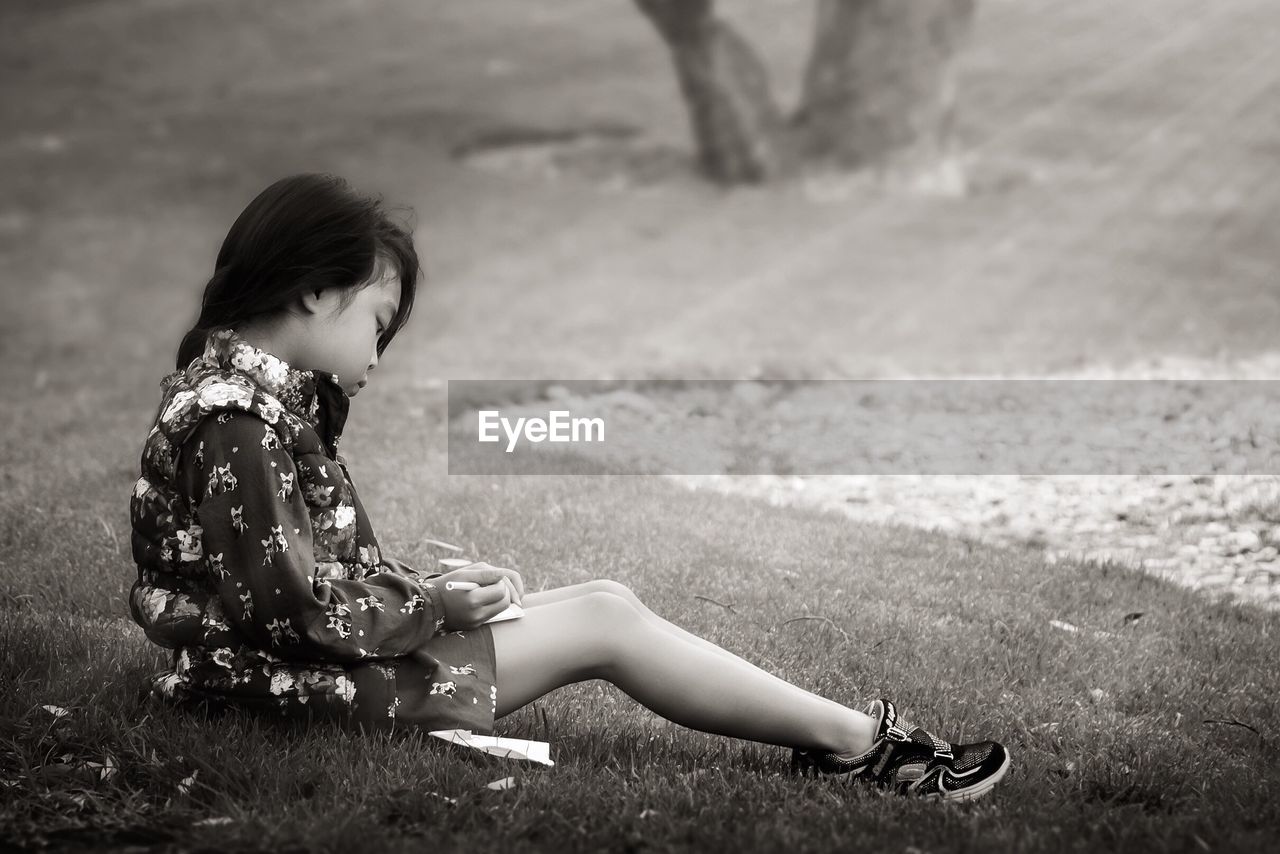 Side view full length of girl sitting on grassy field