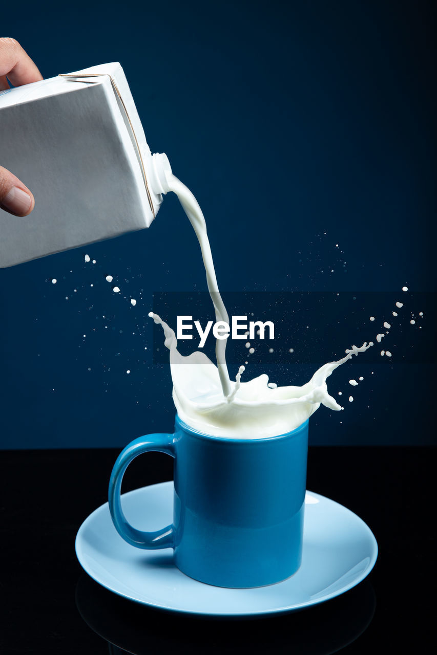 Milk poured into a glass with splash on dark blue background. vertical format.