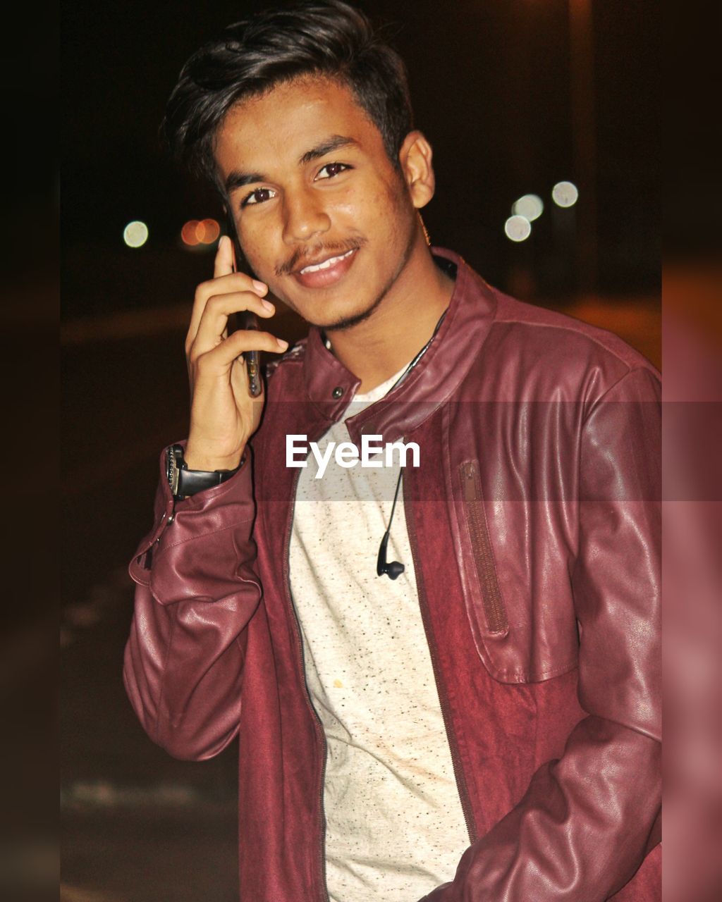 Portrait of young man talking over mobile phone while standing at night